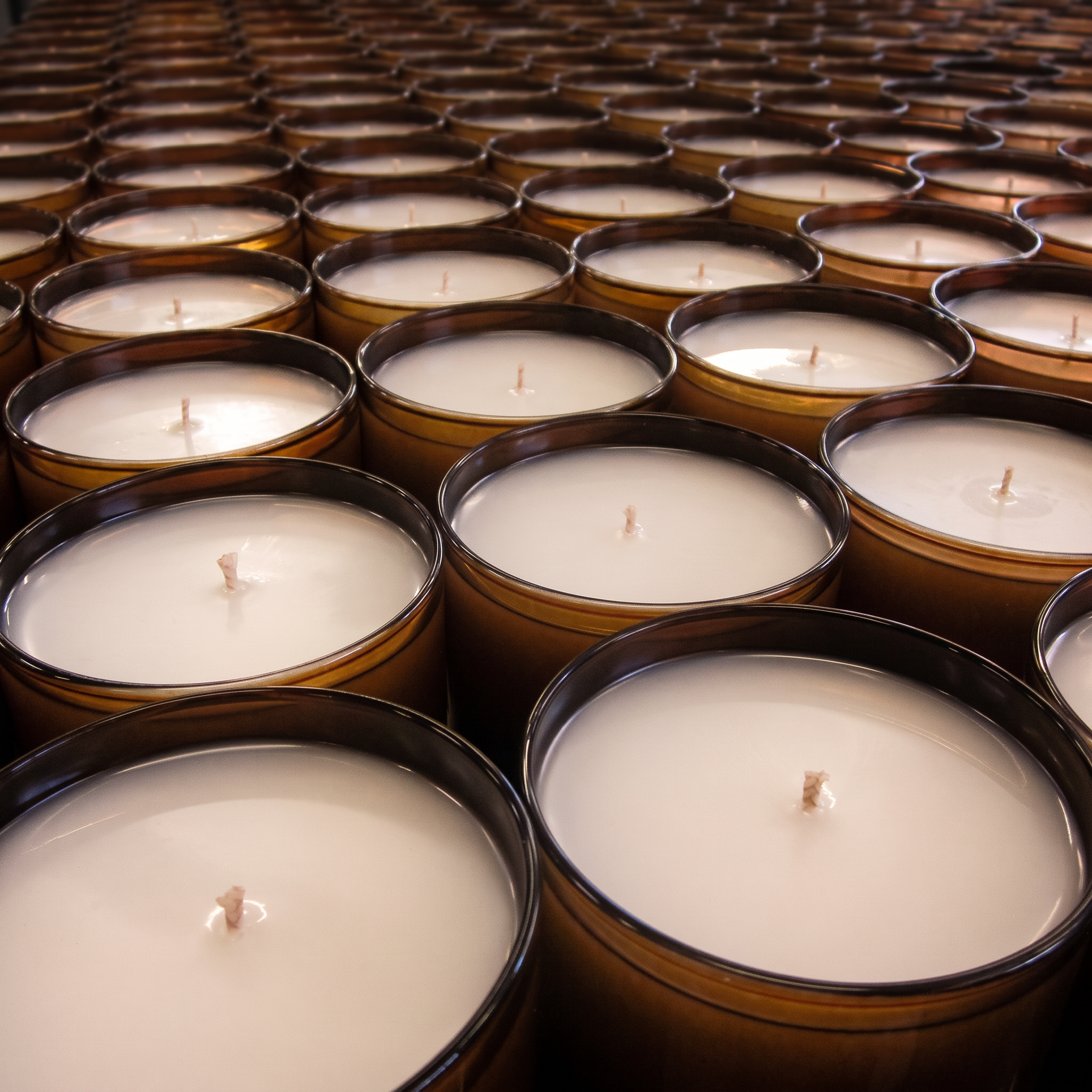 A production run of amber glass candle vessels lined up on a workshop bench