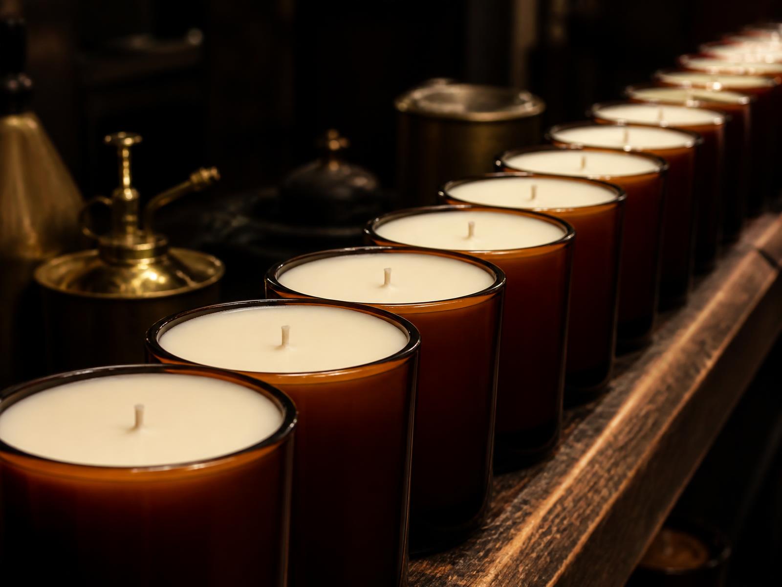 A production run of amber glass candle vessels lined up on a workshop bench